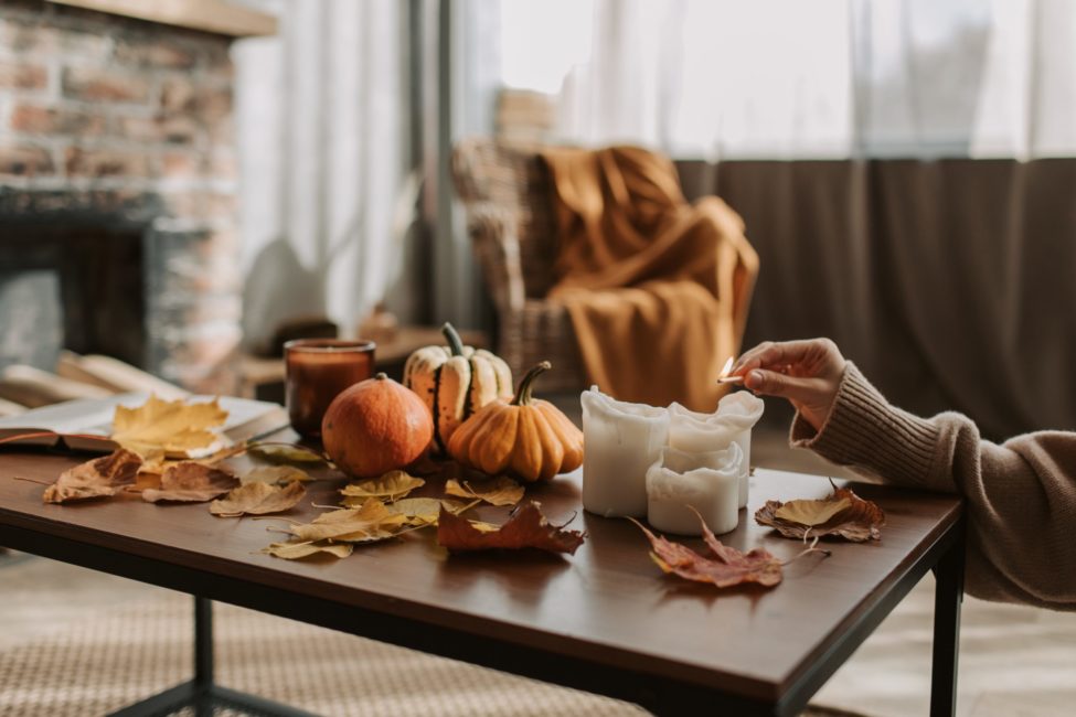 person lighting candle on coffee table with fall decor