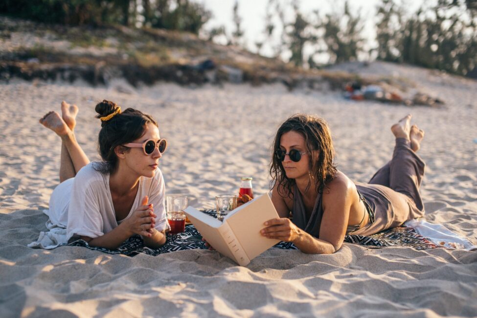 two women laying on beach reading book recommendations newport beach vacation rentals